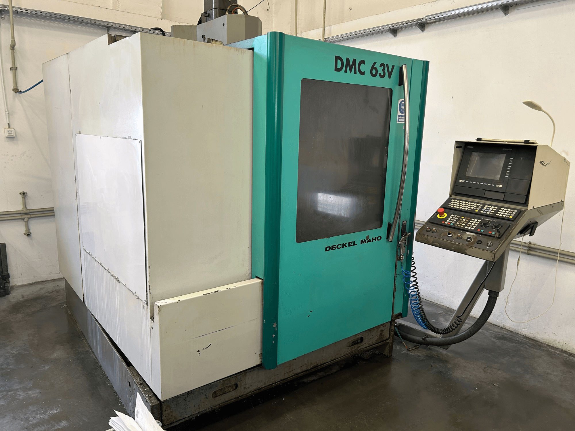 Vertical machining center DECKEL MAHO DMC 63V in a front view, featuring a control panel and blue-green casing.
