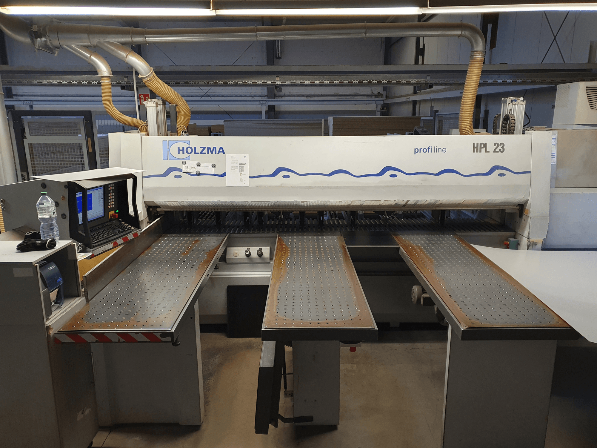 HOLZMA HPL 23 cutting machine shown from the front view, with three perforated tables, computer terminal, and water bottle nearby.