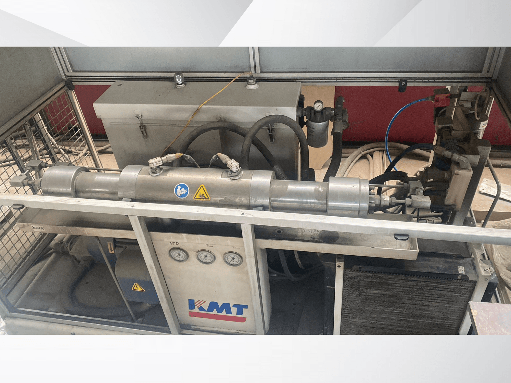 KMT hydraulic machine in front view, featuring pressure gauges, hoses, and a metal casing, ideal for industrial applications.