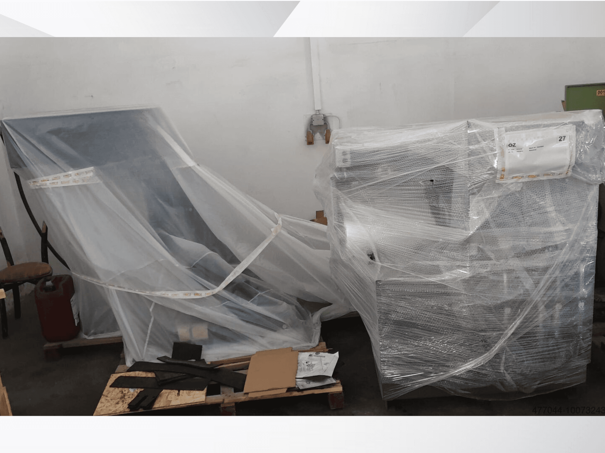 Wrapped industrial equipment in plastic, featuring a chair and machine, viewed from a side angle in a warehouse setting.