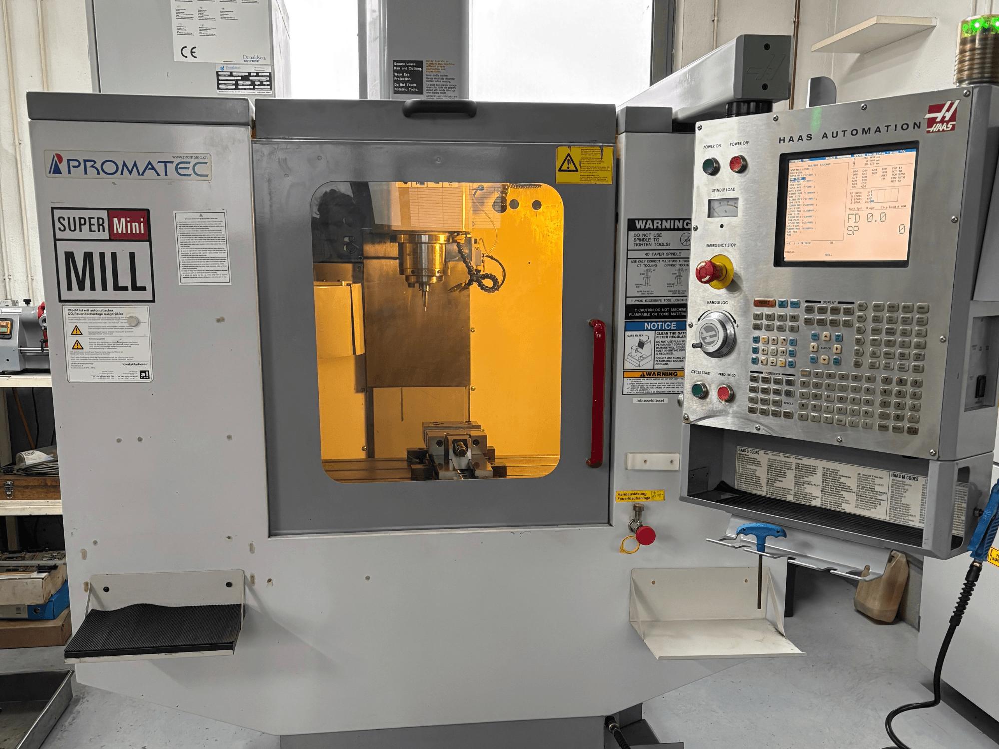Promatec Super Mini Mill in front view, equipped with a Haas Automation control panel and visible cutting tool inside.