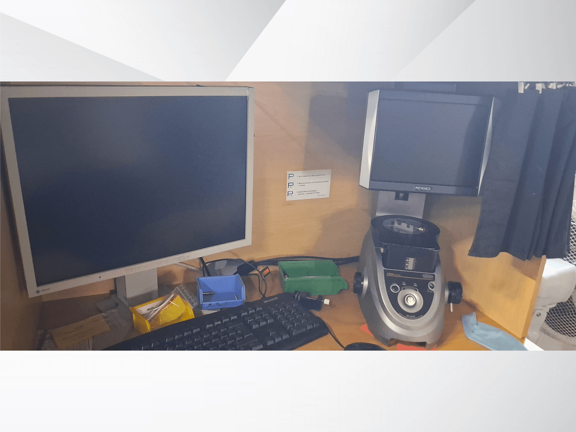 Computer monitor with keyboard, PEVA brand display, and a gray lab device on a wooden desk with assorted trays and paperwork.