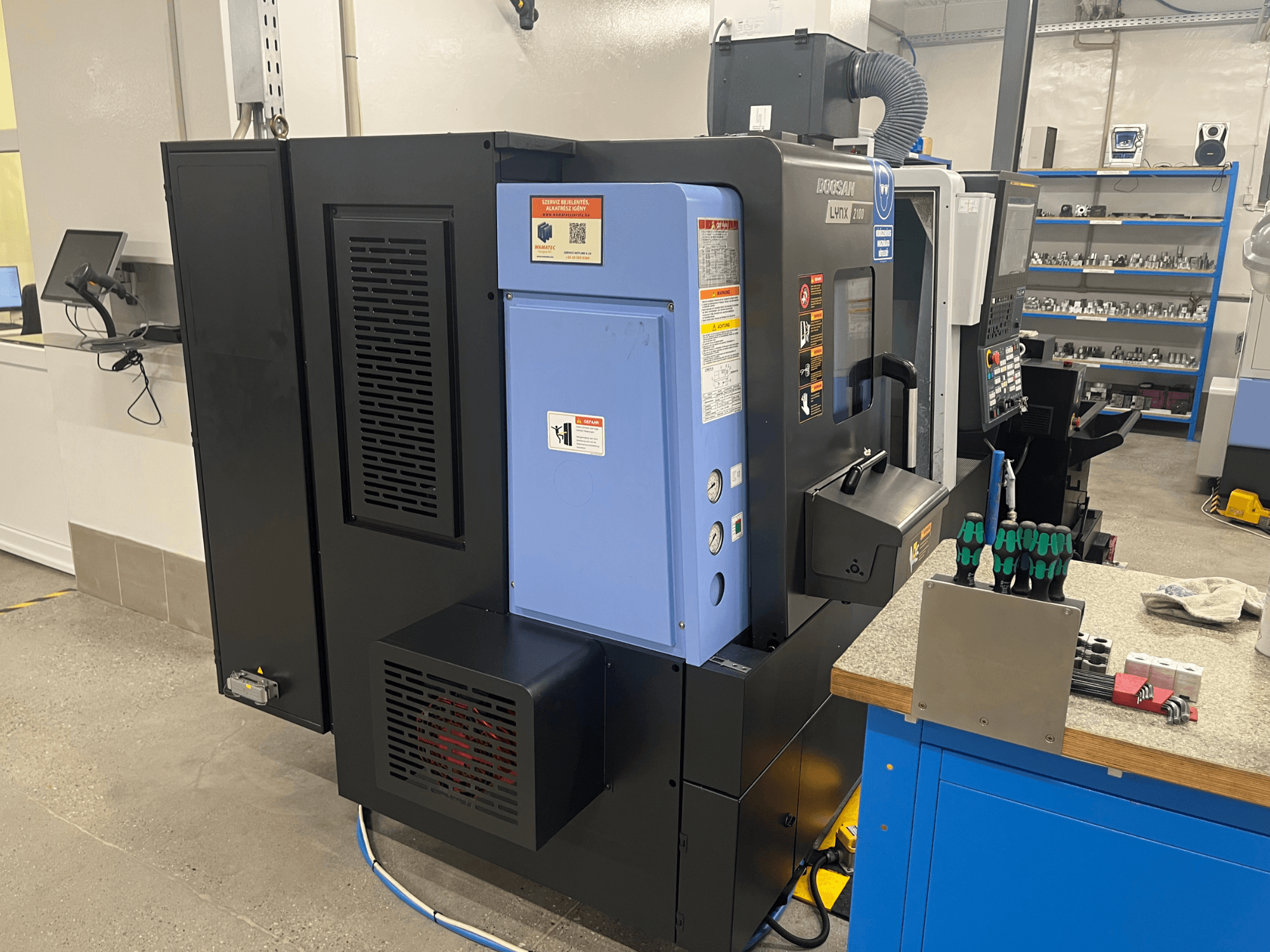 Doosan Lynx 2100 lathe, side view, showcasing control panel, ventilation system, and tools on a workbench.