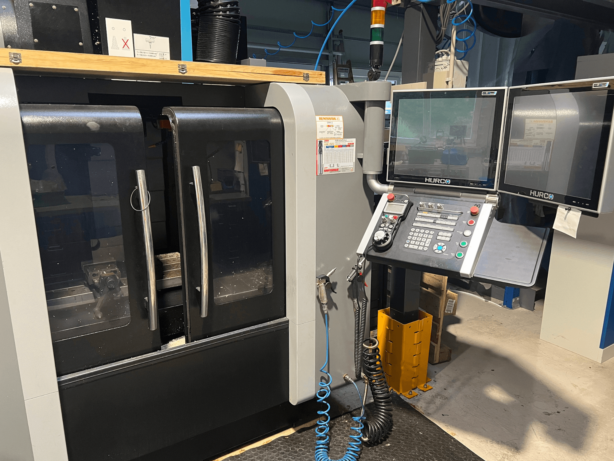 Hurco CNC machine front view with dual monitors and control panel. Features clear doors and visible machining area inside.