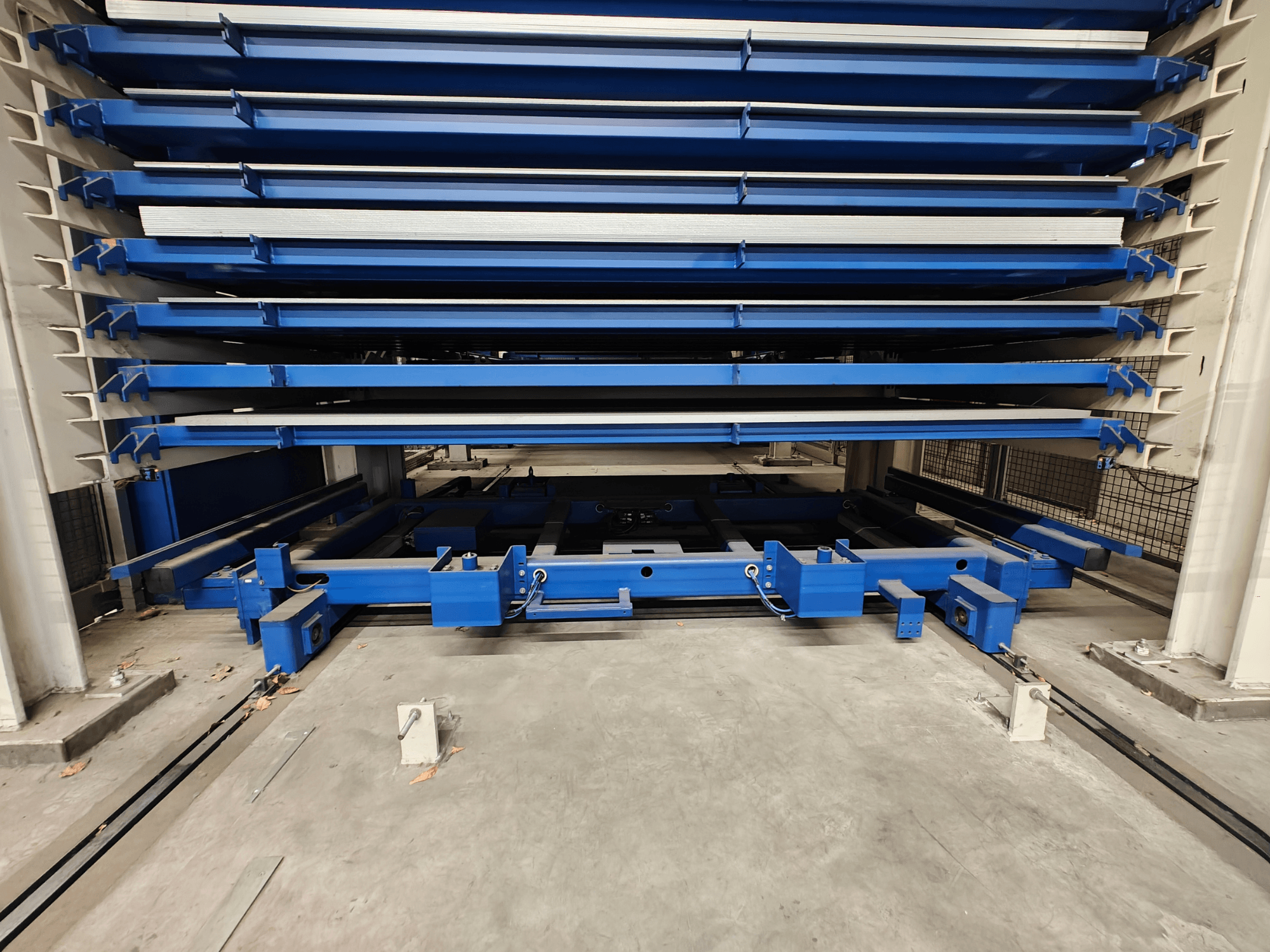 Blue industrial storage rack with multiple horizontal shelves, viewed from the front. Features lifting mechanism and support beams.