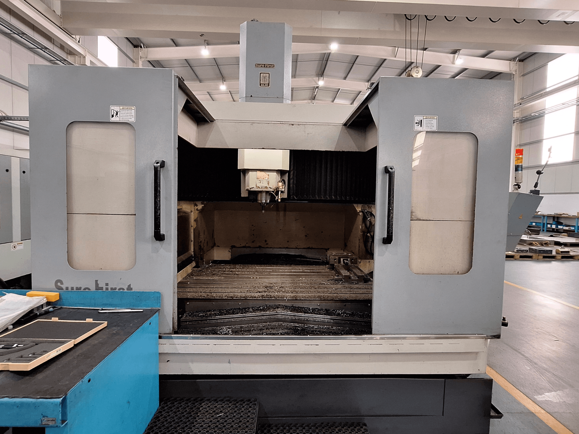 Vertical machining center Sure First QM-1836, front view showing tool head and empty work area, modern industrial setting.