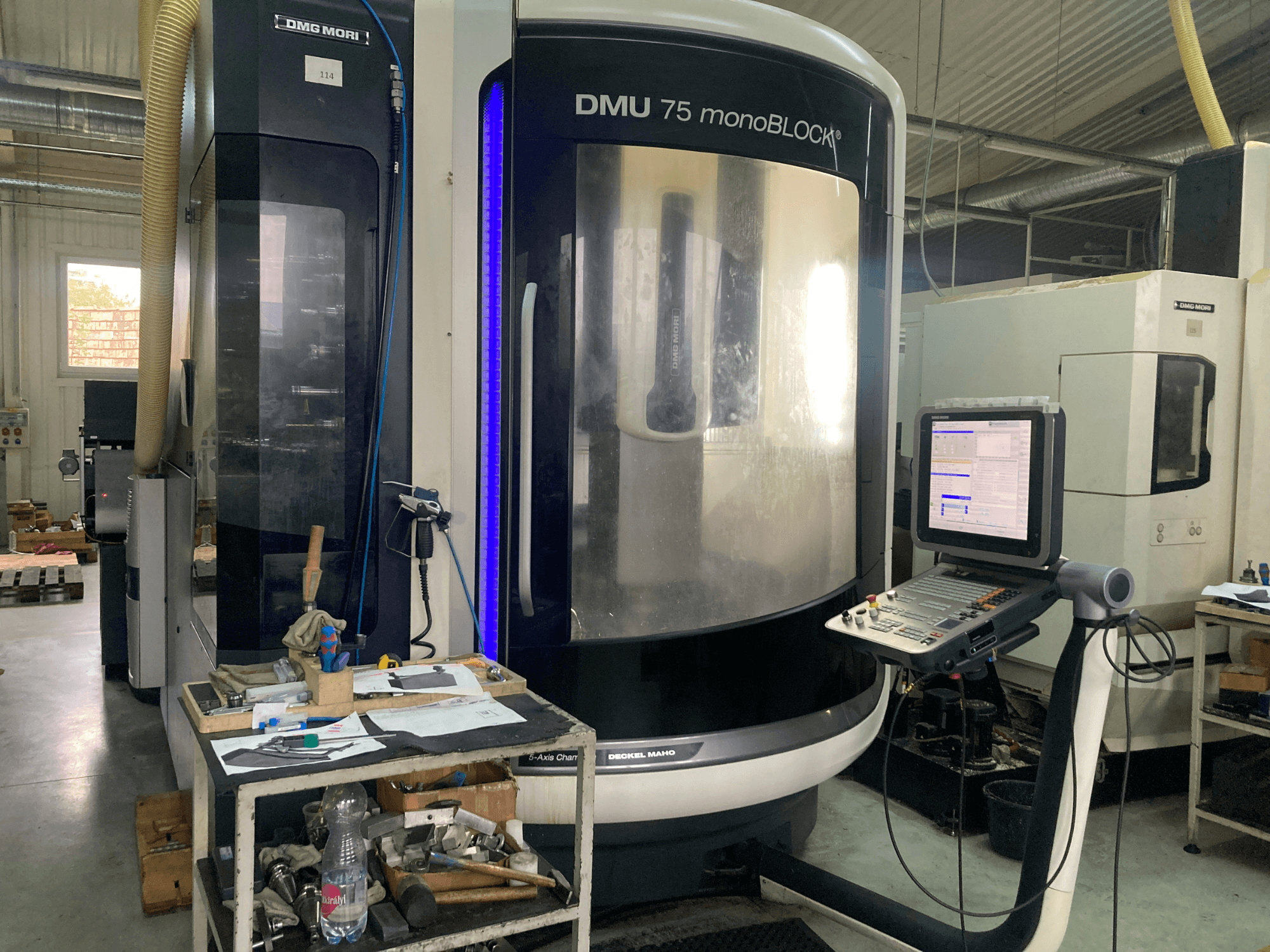 DMG MORI DMU 75 monoBLOCK® CNC machine, front view, featuring control panel, tools, and a workspace with materials.