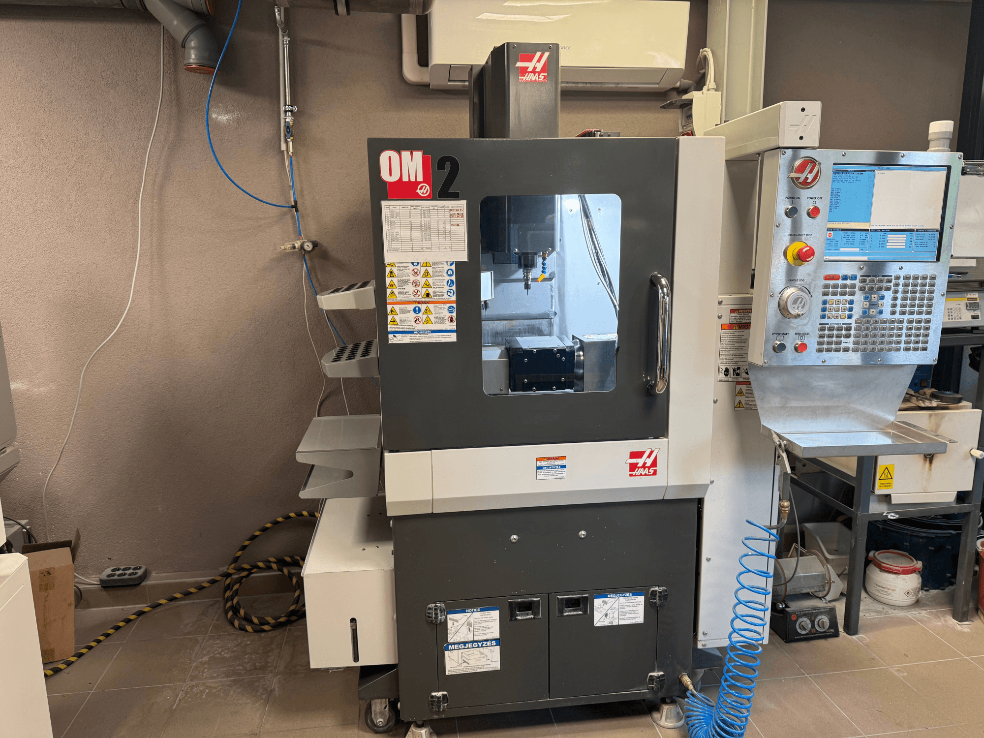 Haas OM-2 CNC machine, front view, features control panel, spindle, and safety labels, set in a workshop environment.