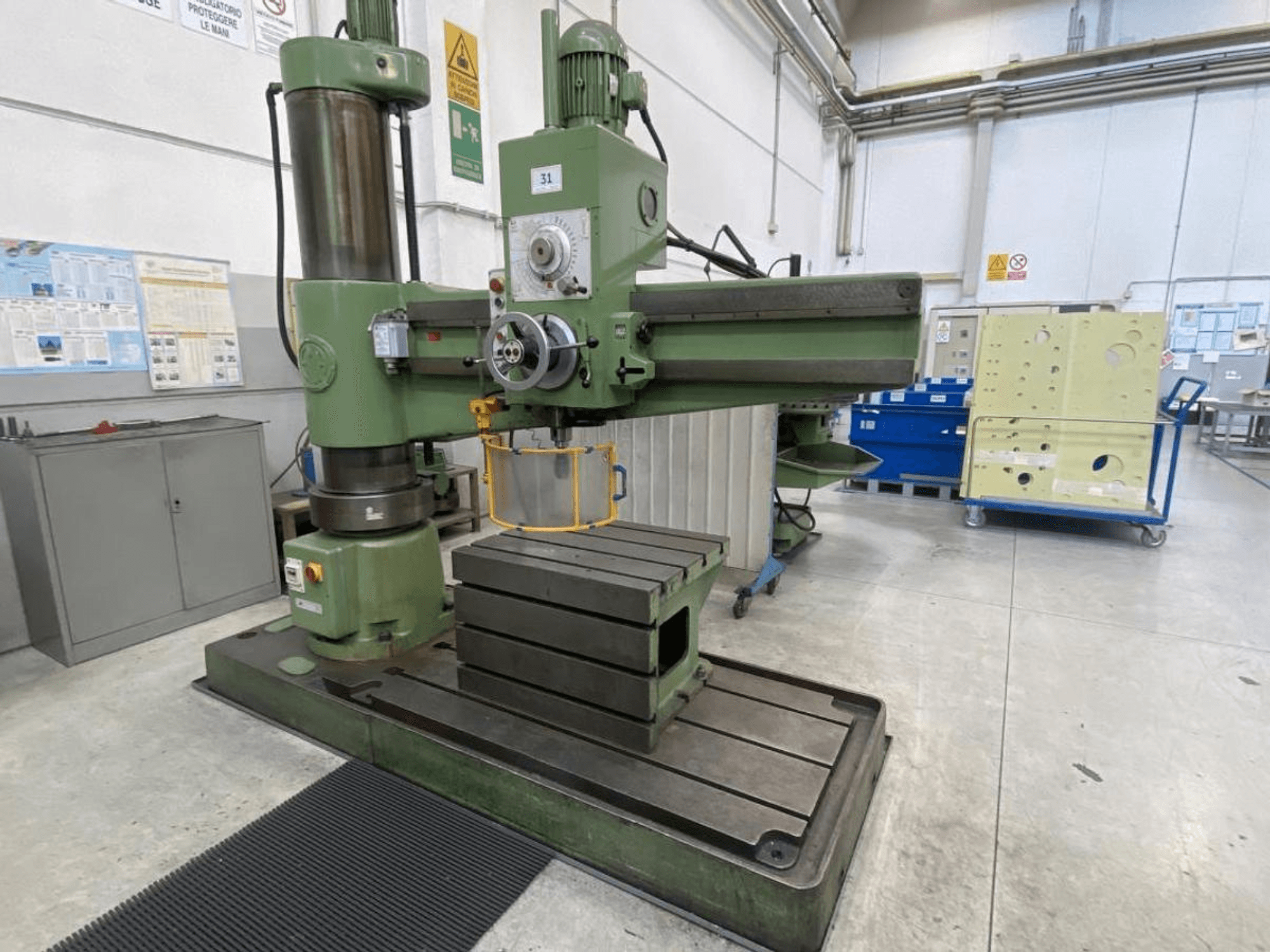 Green vertical milling machine with a large rectangular table, front view, showcasing tooling and control panel, in a workshop setting.