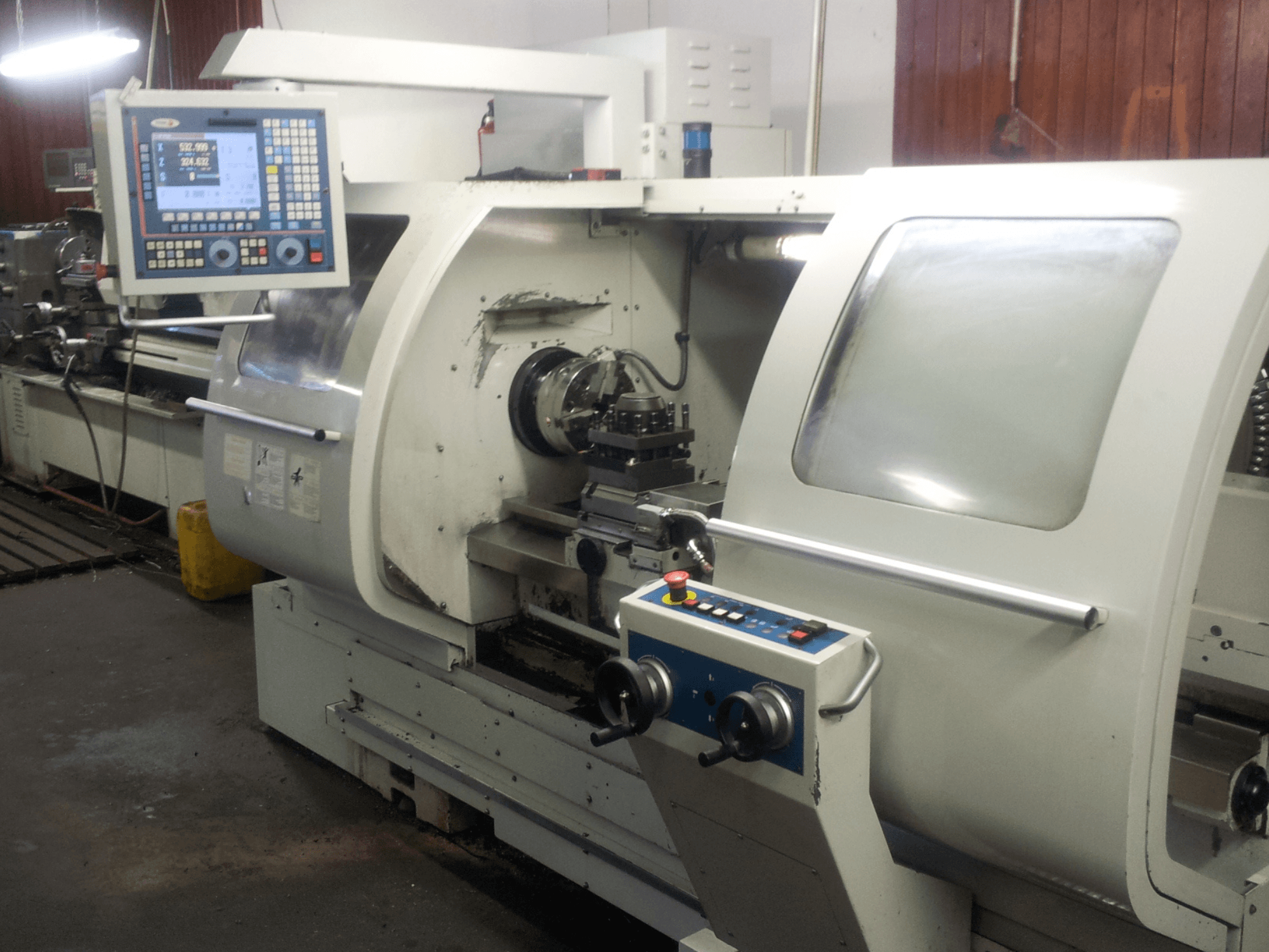 Front view of a CNC lathe with a digital control panel, highlighting the chuck, spindle, and safety features.