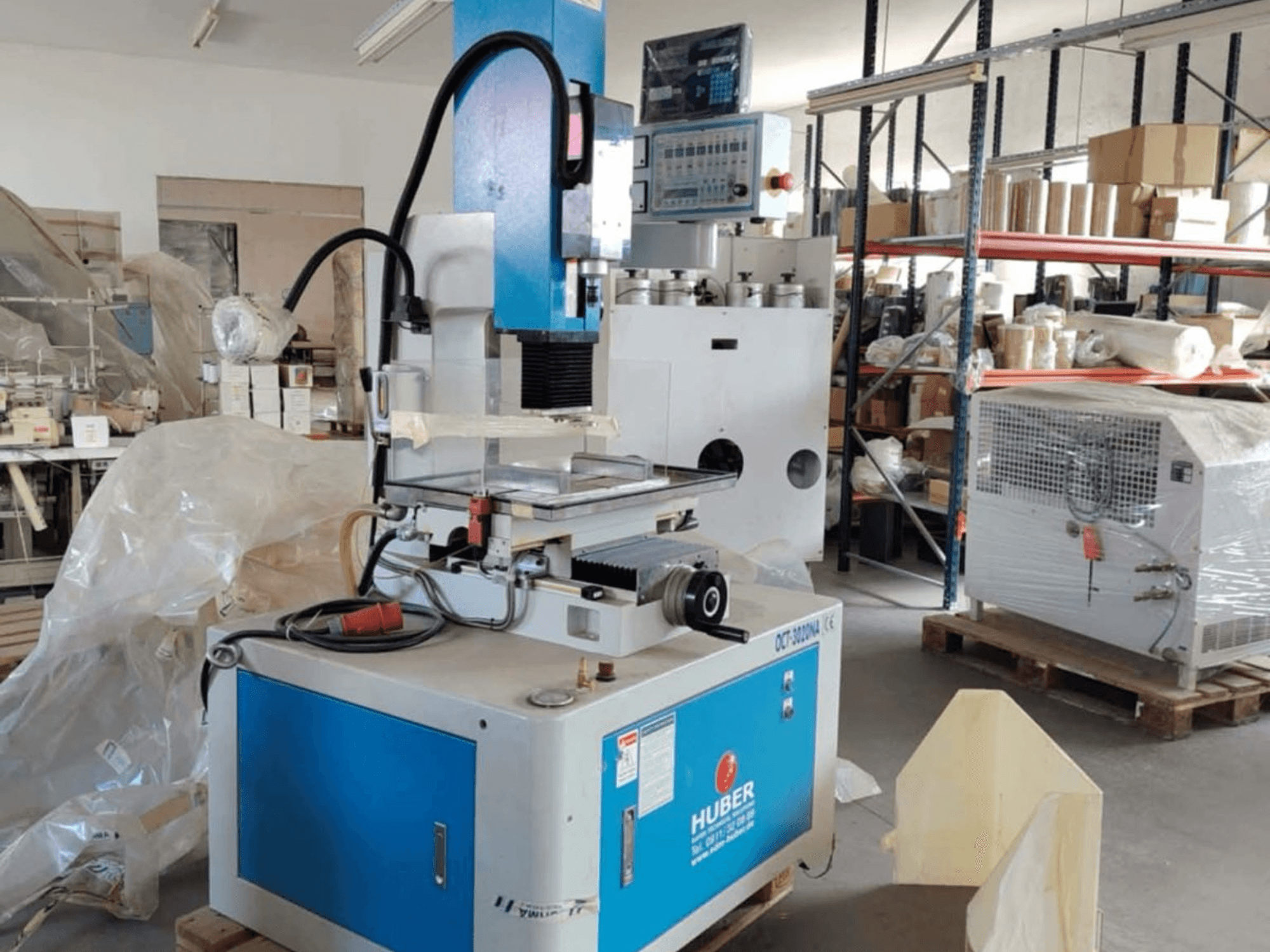 HUBER OCT-3020 NA die-sinking EDM machine in a workshop, front view showing blue and gray casing, digital controls, and work area.