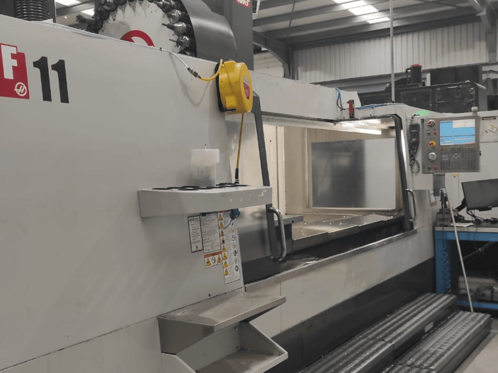 Machinery from Haas, model VF-11, shown from a front view with control panel, large work area, and safety labels visible.