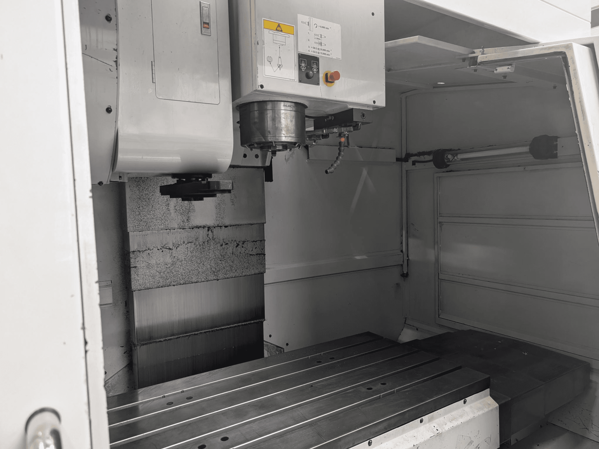 Inside view of a CNC milling machine with a large metal worktable and spindle motor, showing detailed components and control panel.