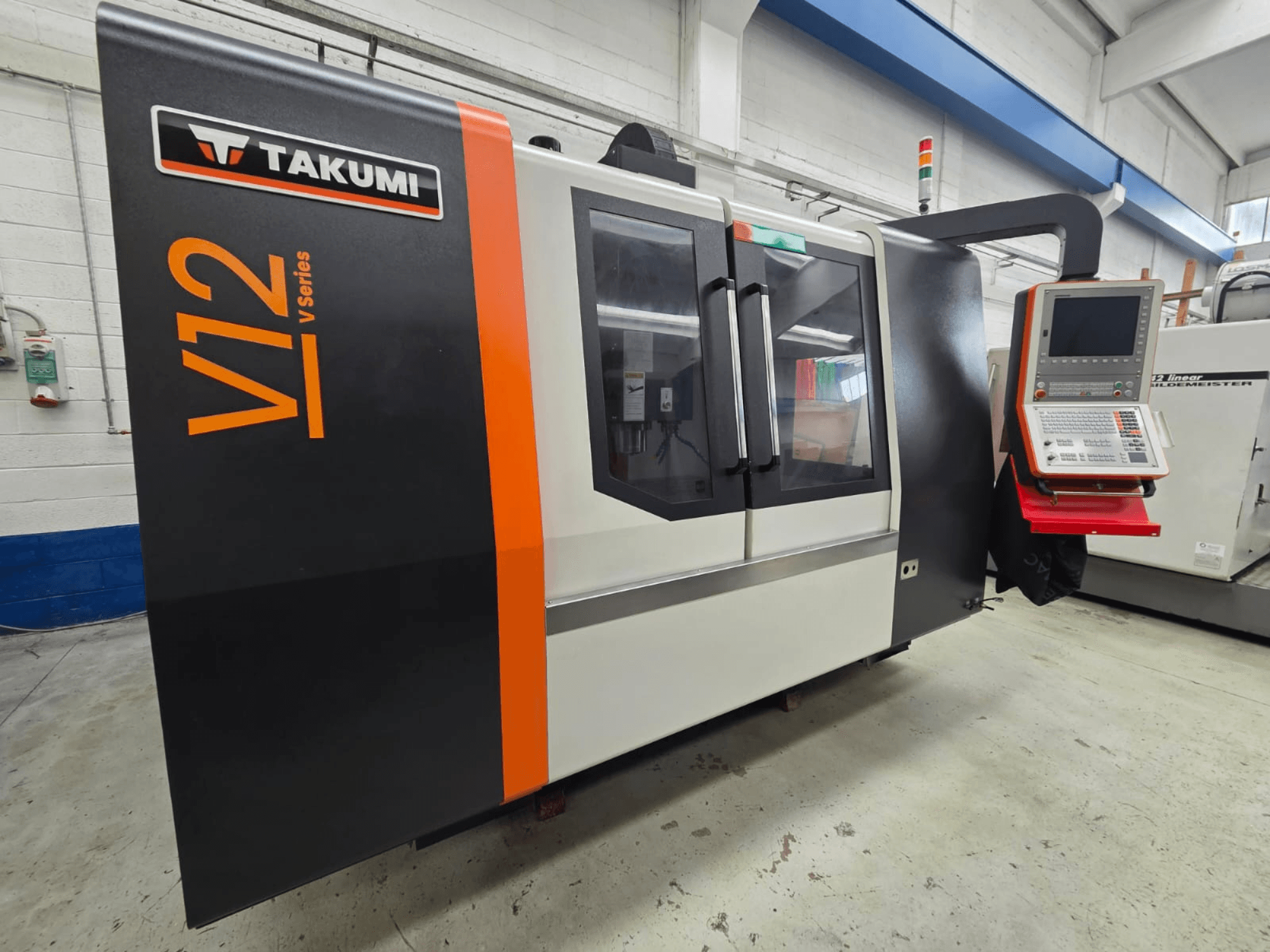 Takumi V12 V series CNC milling machine, front view, features a control panel and large glass windows.