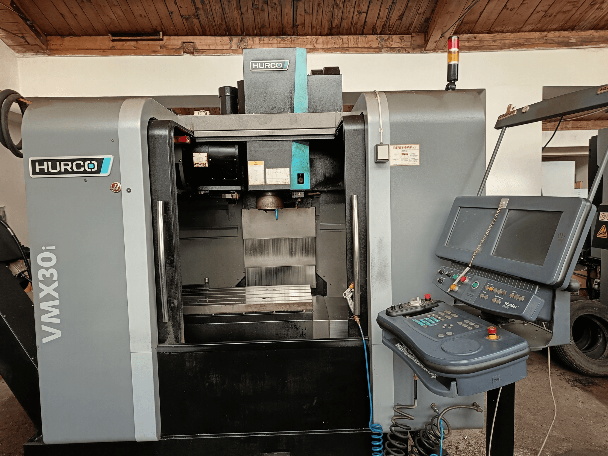 HURCO VMX30i machining center in front view, featuring control panel with buttons and monitor, metallic work area, and warning light.