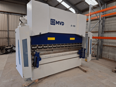 MVD A 100 press brake in a side view, showing controls, safety warnings, and a sturdy metal frame in a spacious workshop.