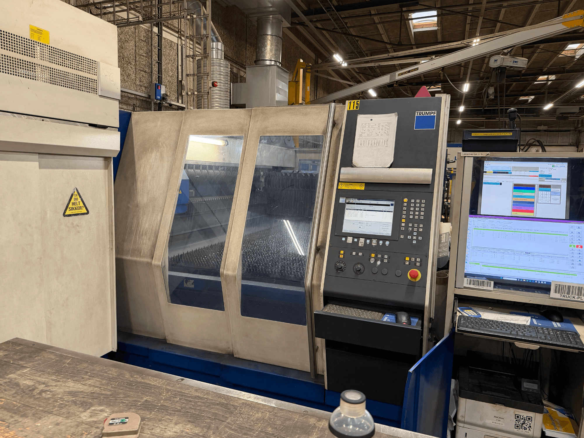 Front view of a Trumpf industrial laser machine with control panel and digital displays, set in a factory environment.