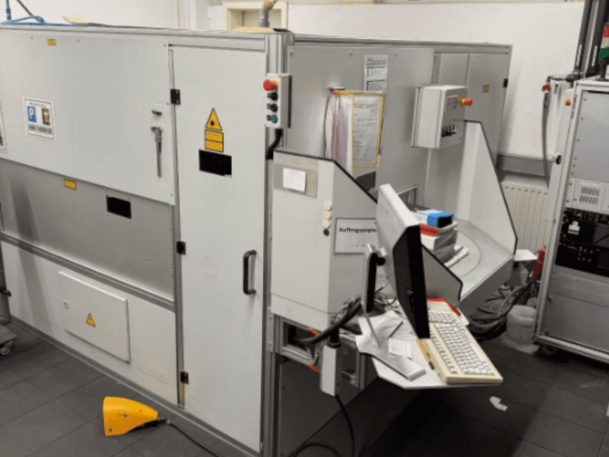 Industrial machine with a computer terminal, side view; includes control buttons and safety warning signs.