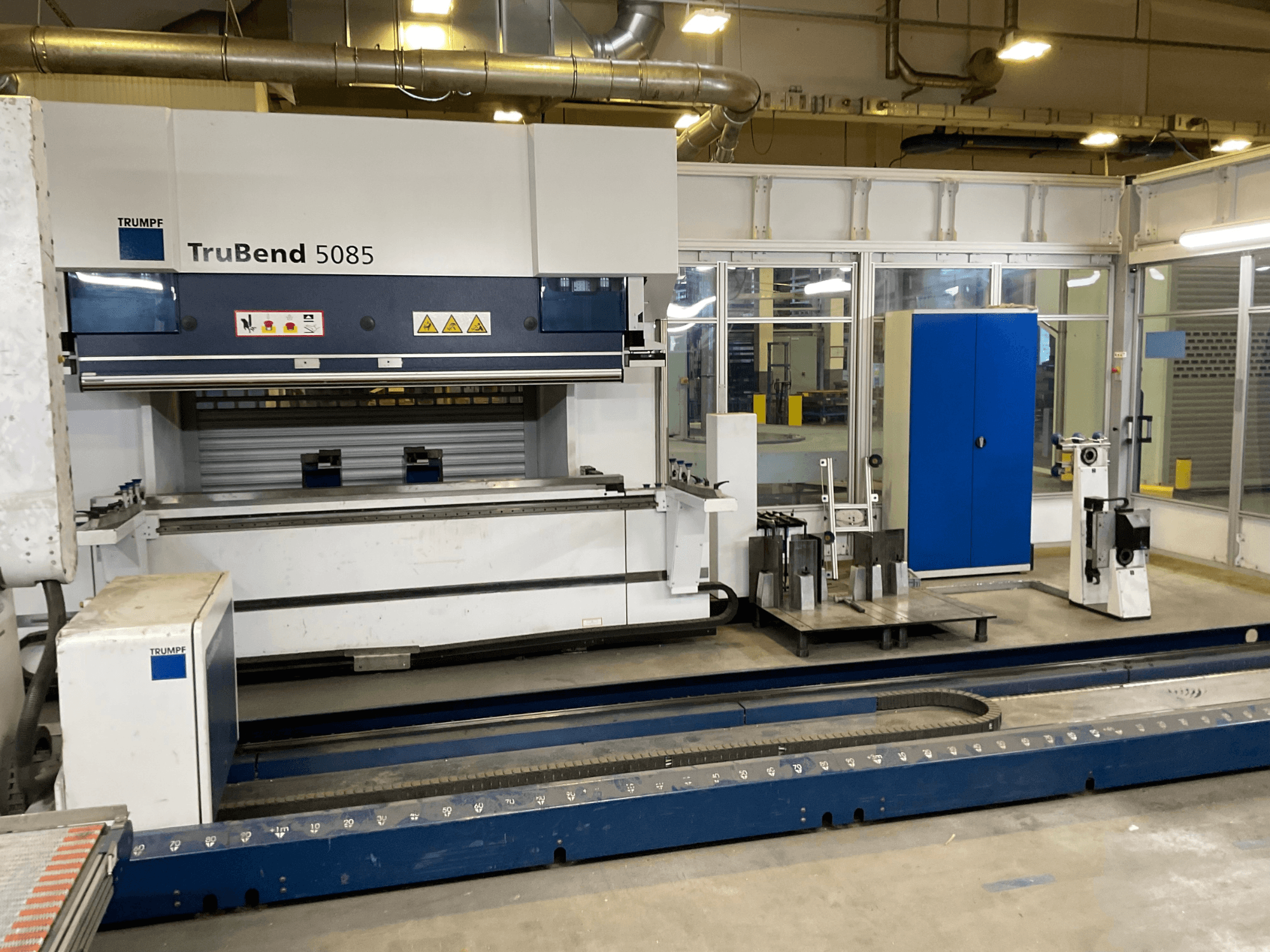 TruBend 5085 by TRUMPF, side view of a large metal bending machine with control panel and various tools beside it.