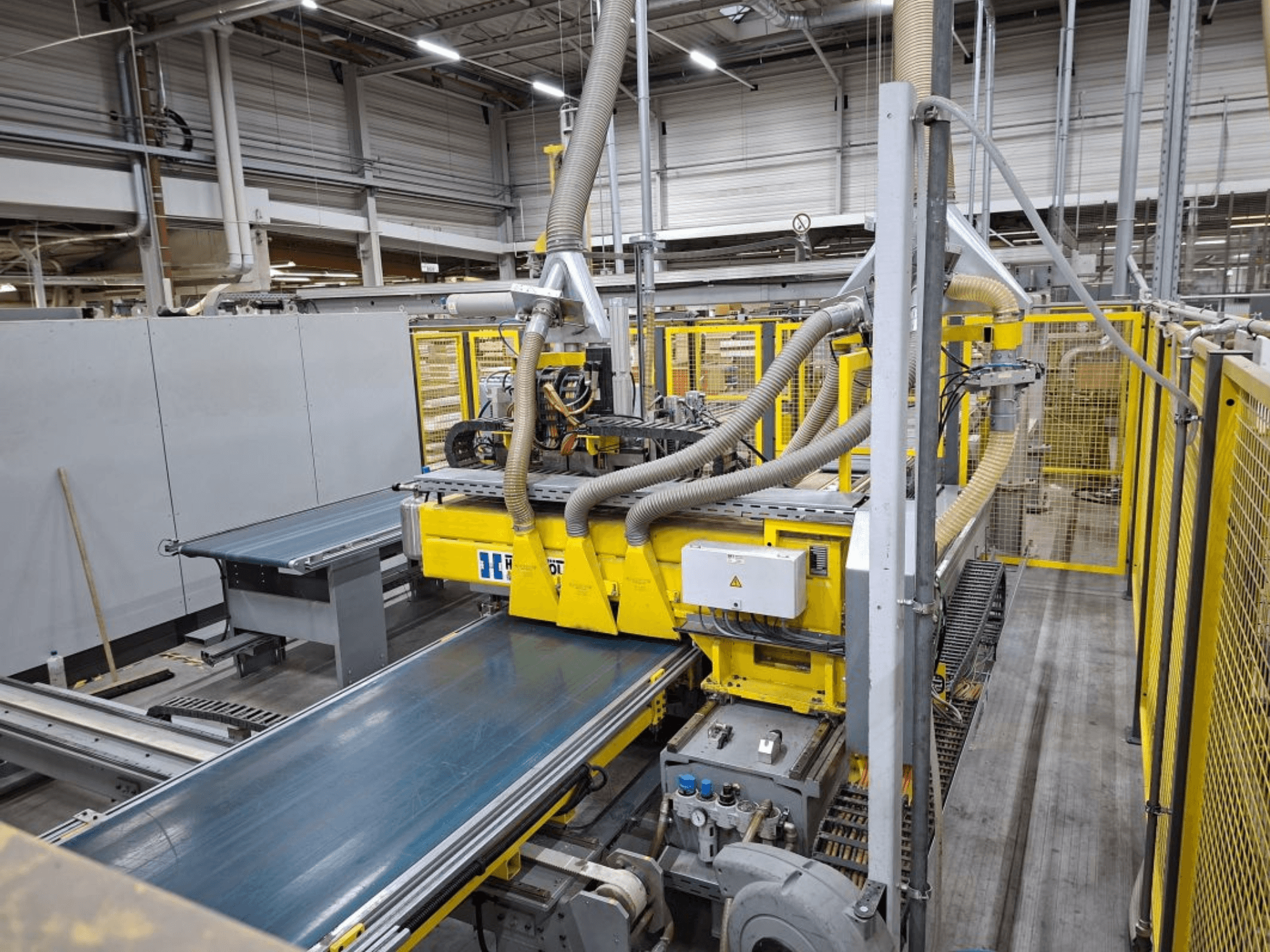 Industrial conveyor system from a side view, featuring yellow machinery, control panel, and hose attachments for manufacturing.