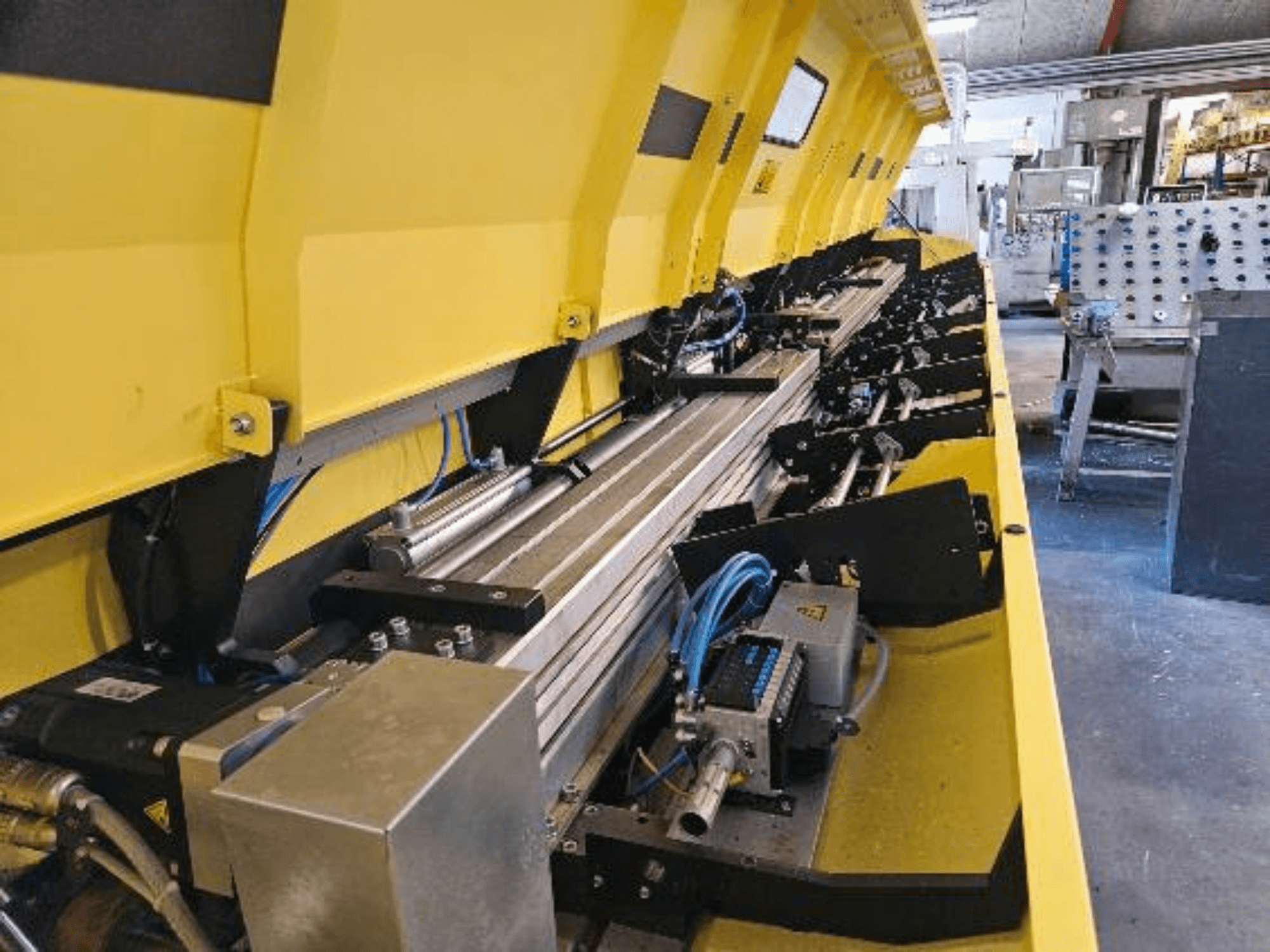 Close-up view of a yellow hydraulic machine with metallic components and conveyor tracks, featuring hoses and electronic parts.