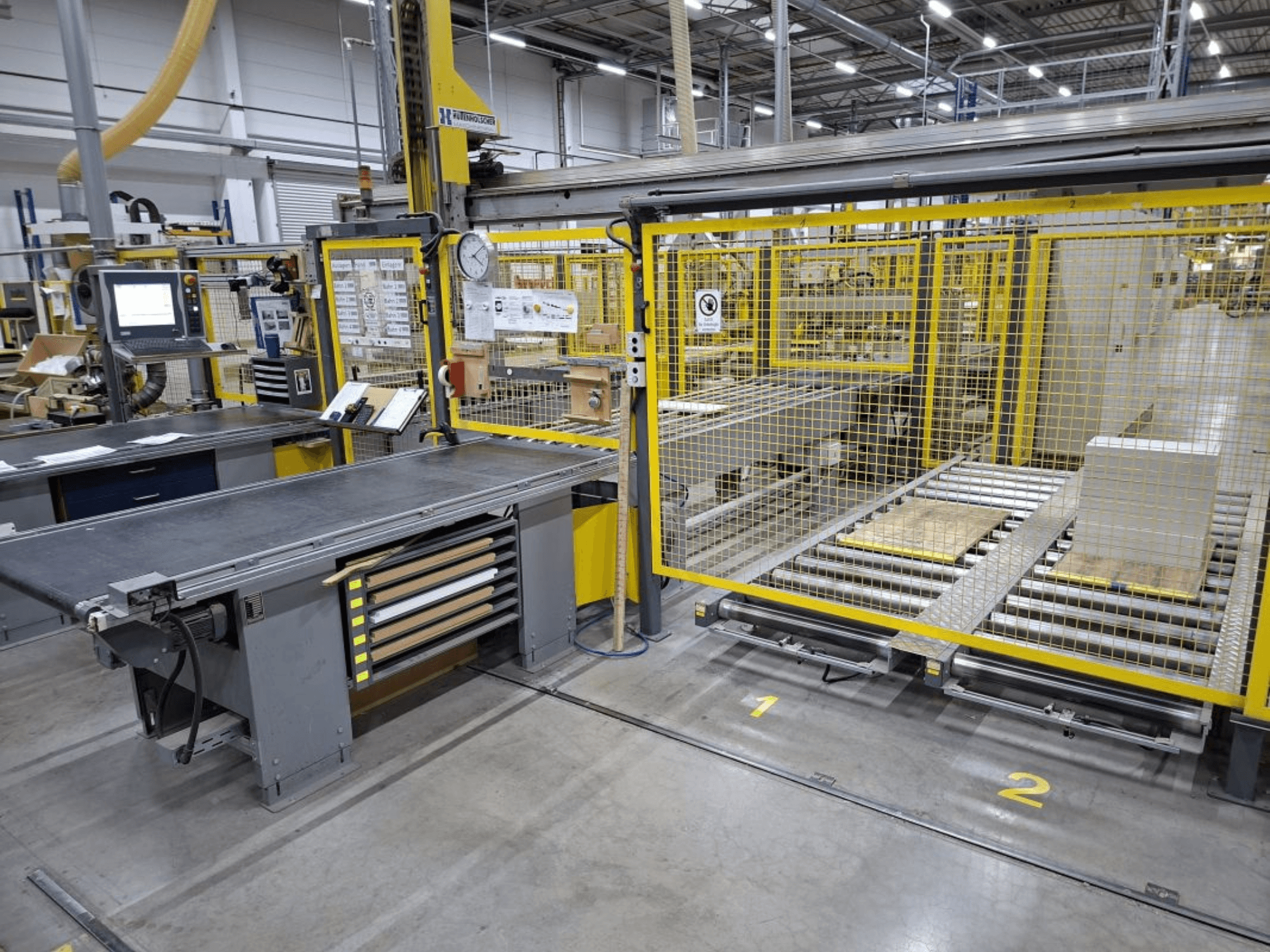 Industrial workspace featuring a conveyor system and control panel; side view showing machinery and safety fencing.
