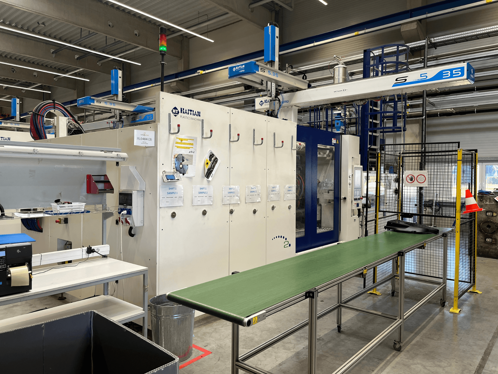 Haitian S5-35 plastic machine in a workshop; green conveyor table, safety barriers, and control panel visible from front view.