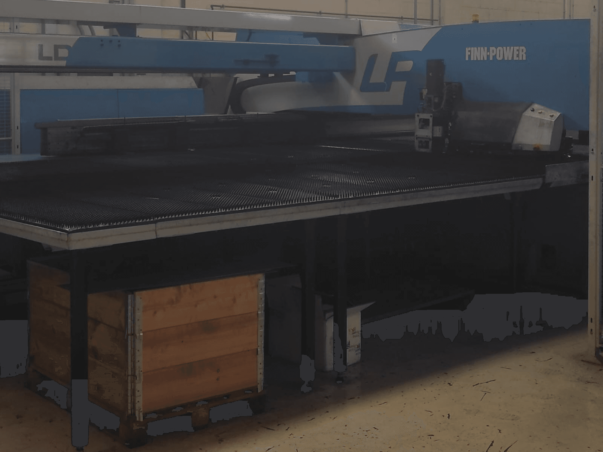 Finn-Power LP cutting machine in a factory, front view with a textured metal table and wooden crate beneath.