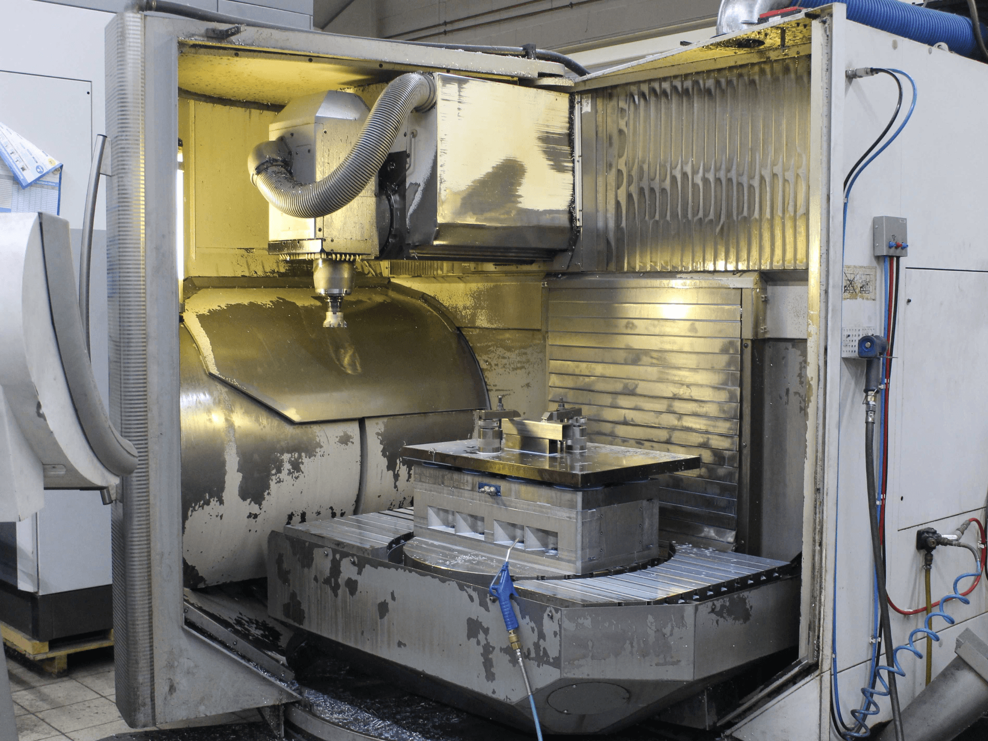 CNC milling machine interior, side view, showcasing workpiece and cutting tool with metal shavings and coolant residue.