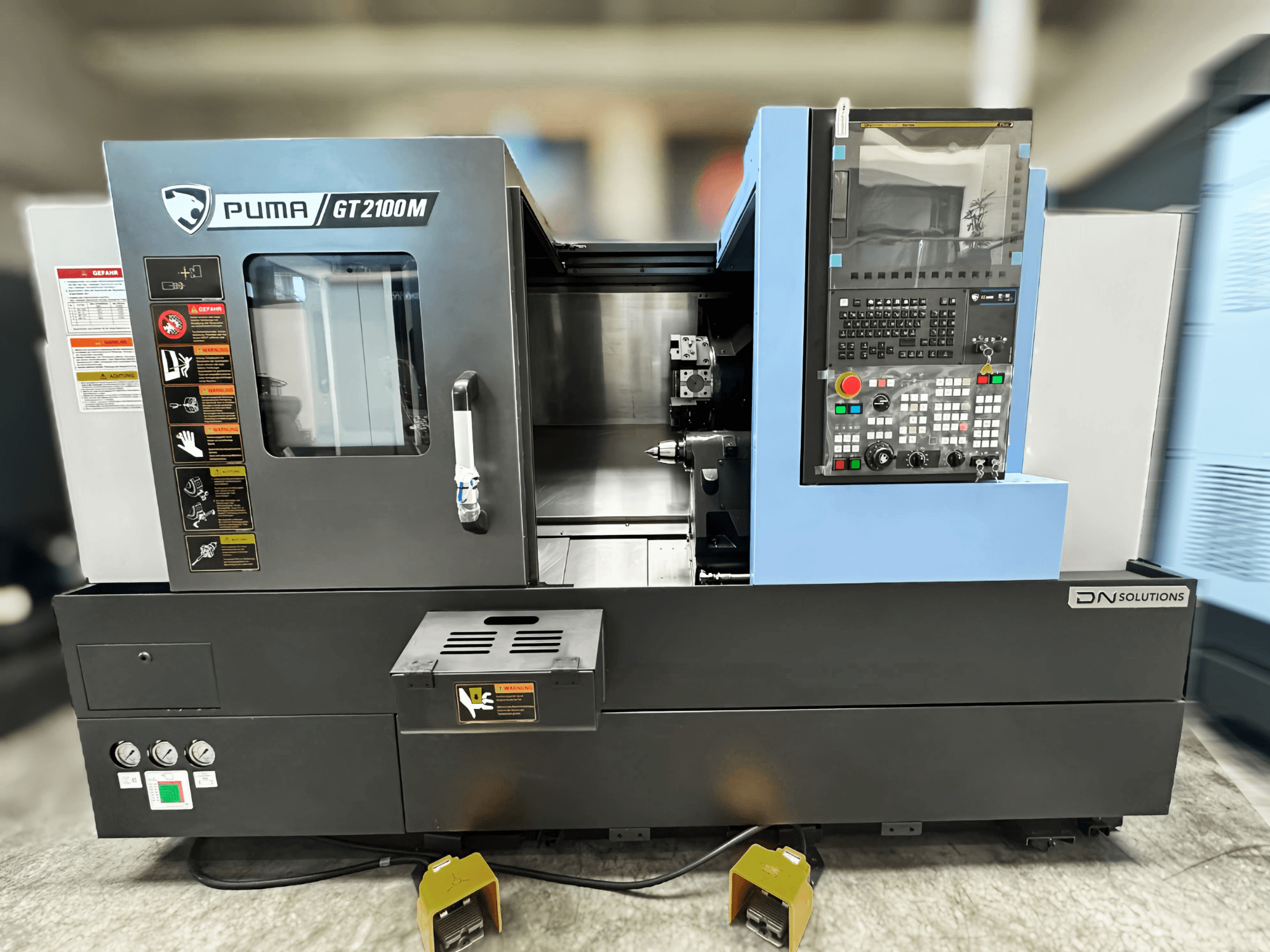 Turn-mill centre DN SOLUTIONS PUMA GT2100M, front view showcasing control panel, machining chamber, and safety labels.