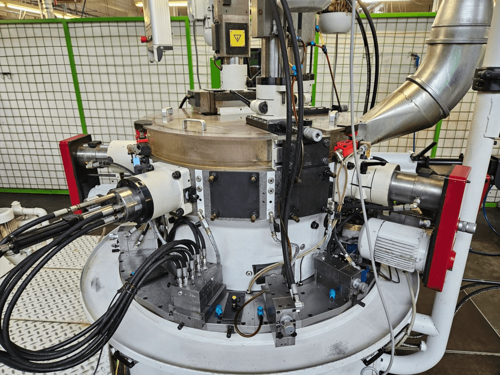 Close-up view of an industrial machine with hydraulic hoses, metal components, and a rotating base. No brand visible.