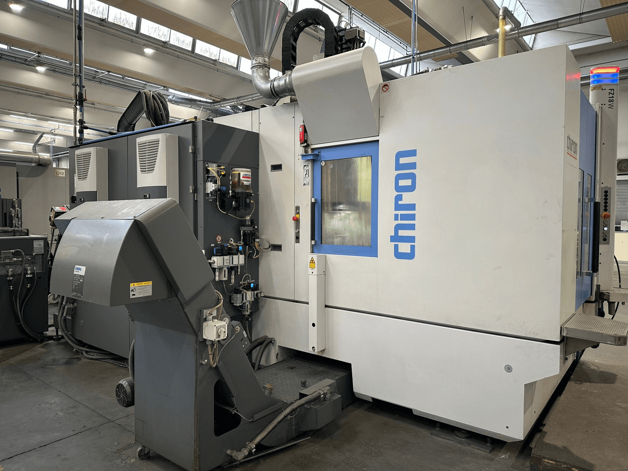 Chiron CNC machine in grey and white, front view, featuring controls, pipes, and a dust extraction hood.