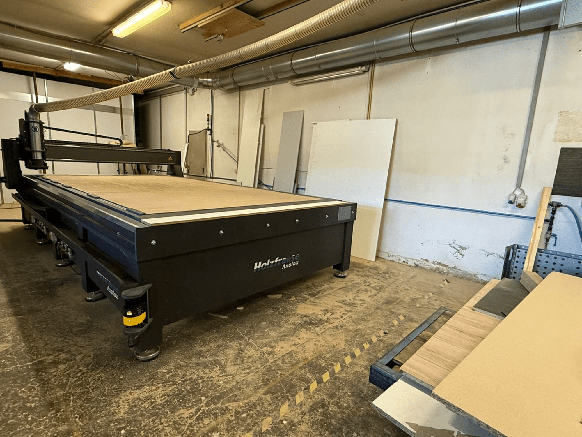Holz-Her Axos 5 CNC router in workshop, front view showing worktable, dust extraction system, and wooden panels nearby.