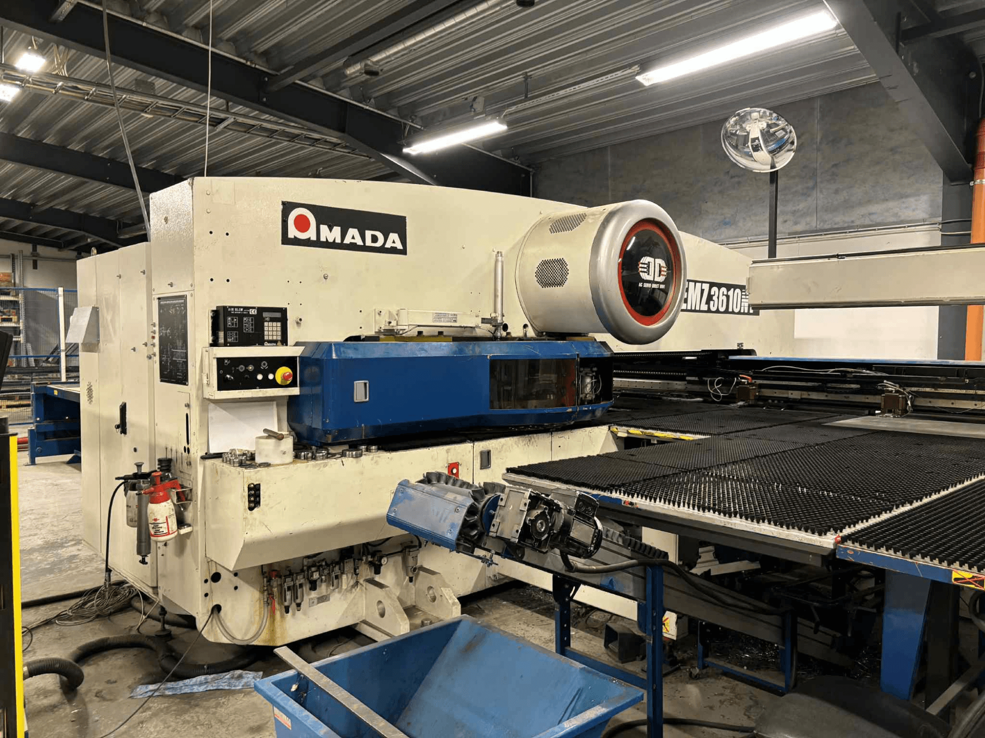Amada EMZ3610H punch press viewed from the front; features operational controls, blue bed, and safety equipment.
