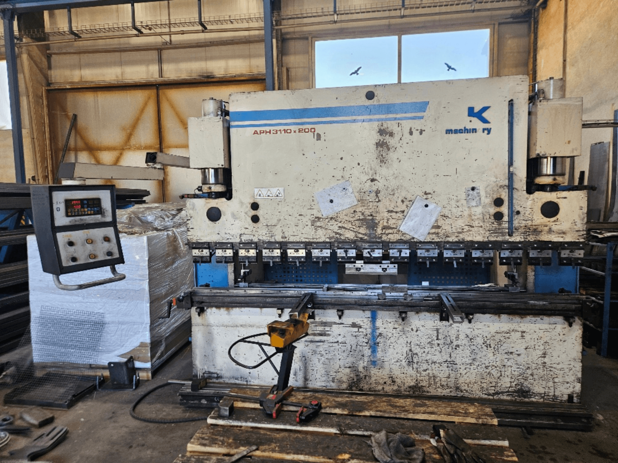 Baykal APH 3110x200 press brake in a workshop, front view, with control panel, metal sheets, and tools visible.