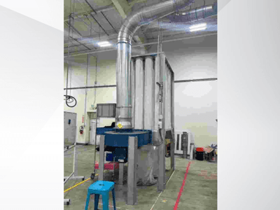 Large industrial ventilation system, front view, with shiny metal ducting and a blue base, situated in a spacious warehouse.