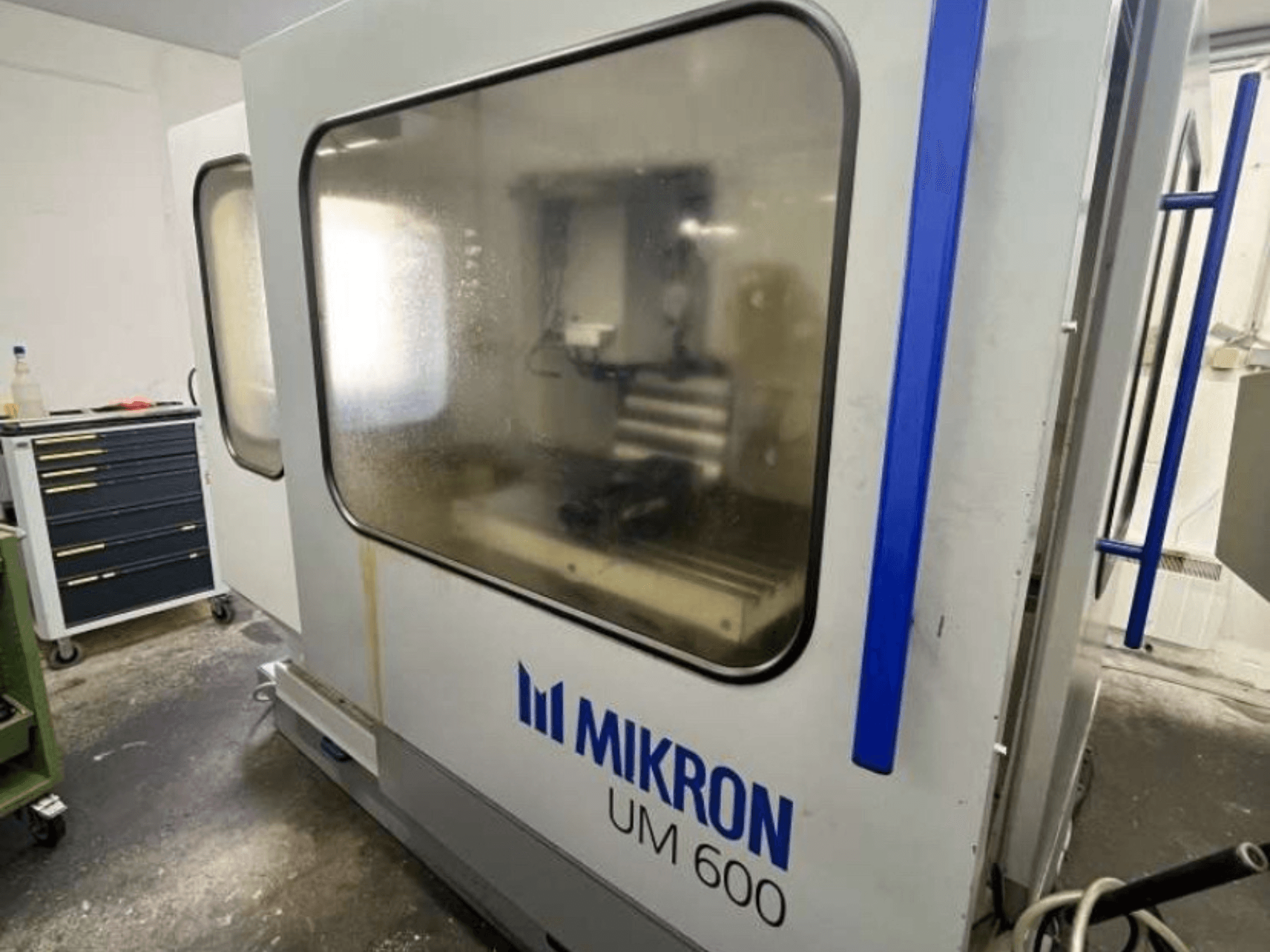 MIKRON UM 600 TNC 410/426 universal machining center, side view, with fogged glass and visible tool storage nearby.