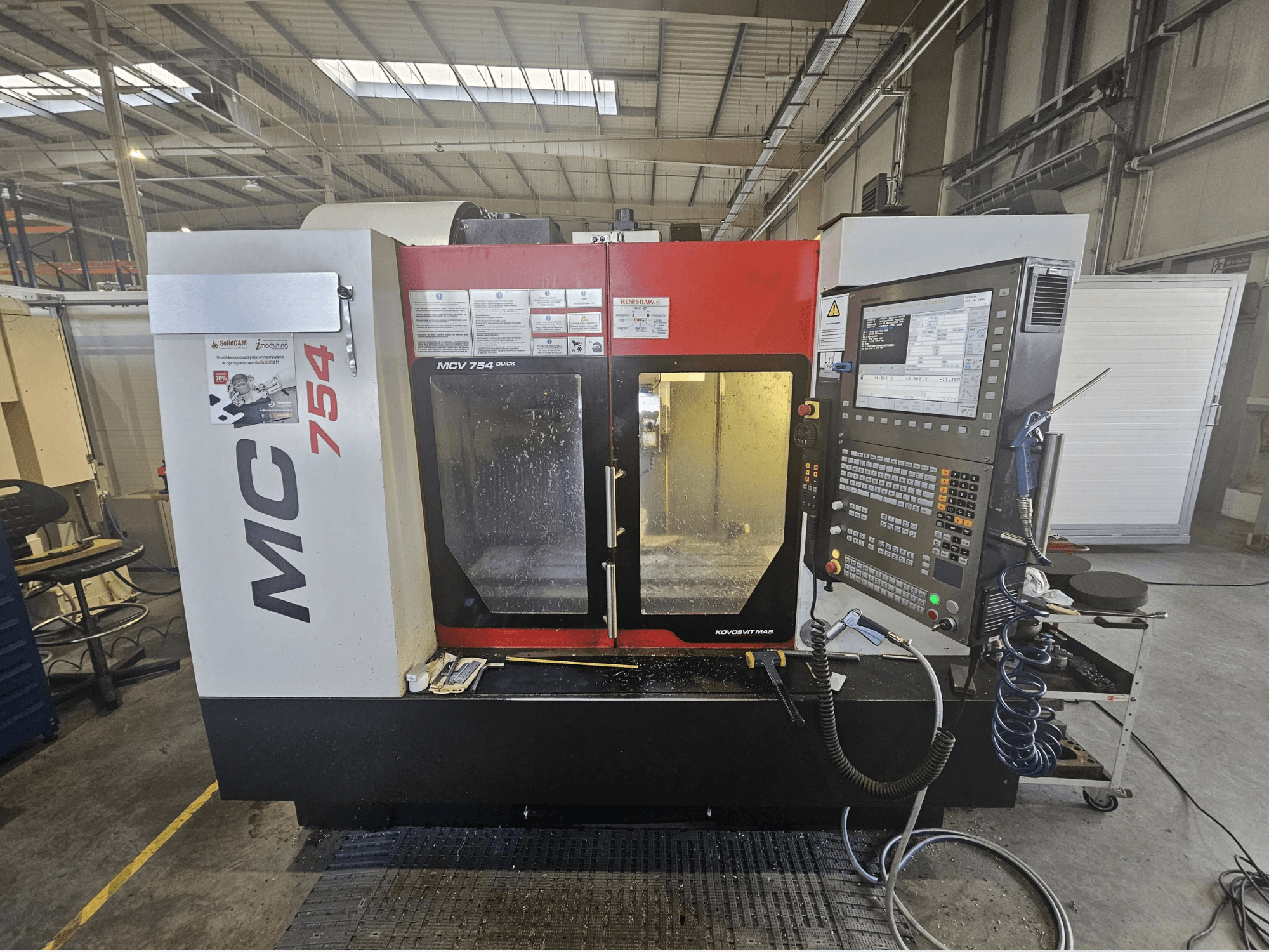 MC 754 CNC milling machine in a front view, features a control panel with buttons, screens, and a work area with coolant.
