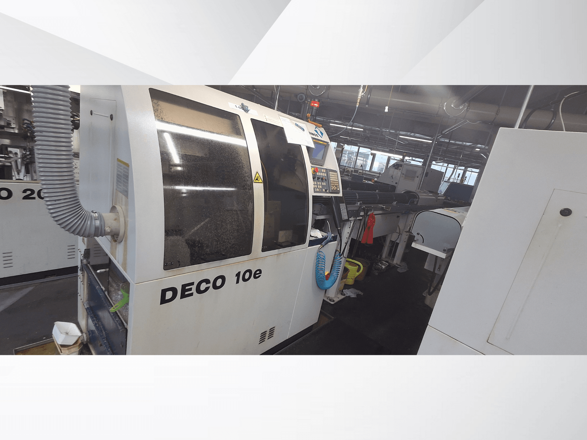 DECO 10e machine in a workshop; side view showing control panel and ventilation hose, with blurred machinery in the background.