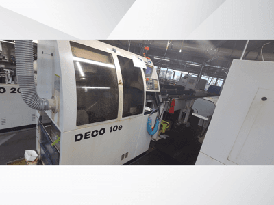 DECO 10e machine in a workshop; side view showing control panel and ventilation hose, with blurred machinery in the background.