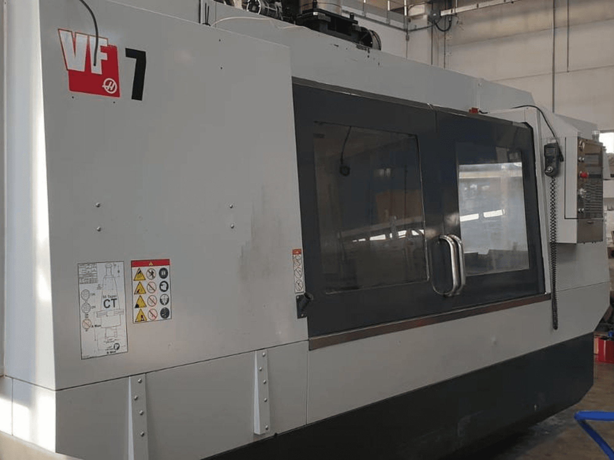 Haas VF-7 CNC machine in side view, showcasing a metal grey finish, control panel, and safety labels.
