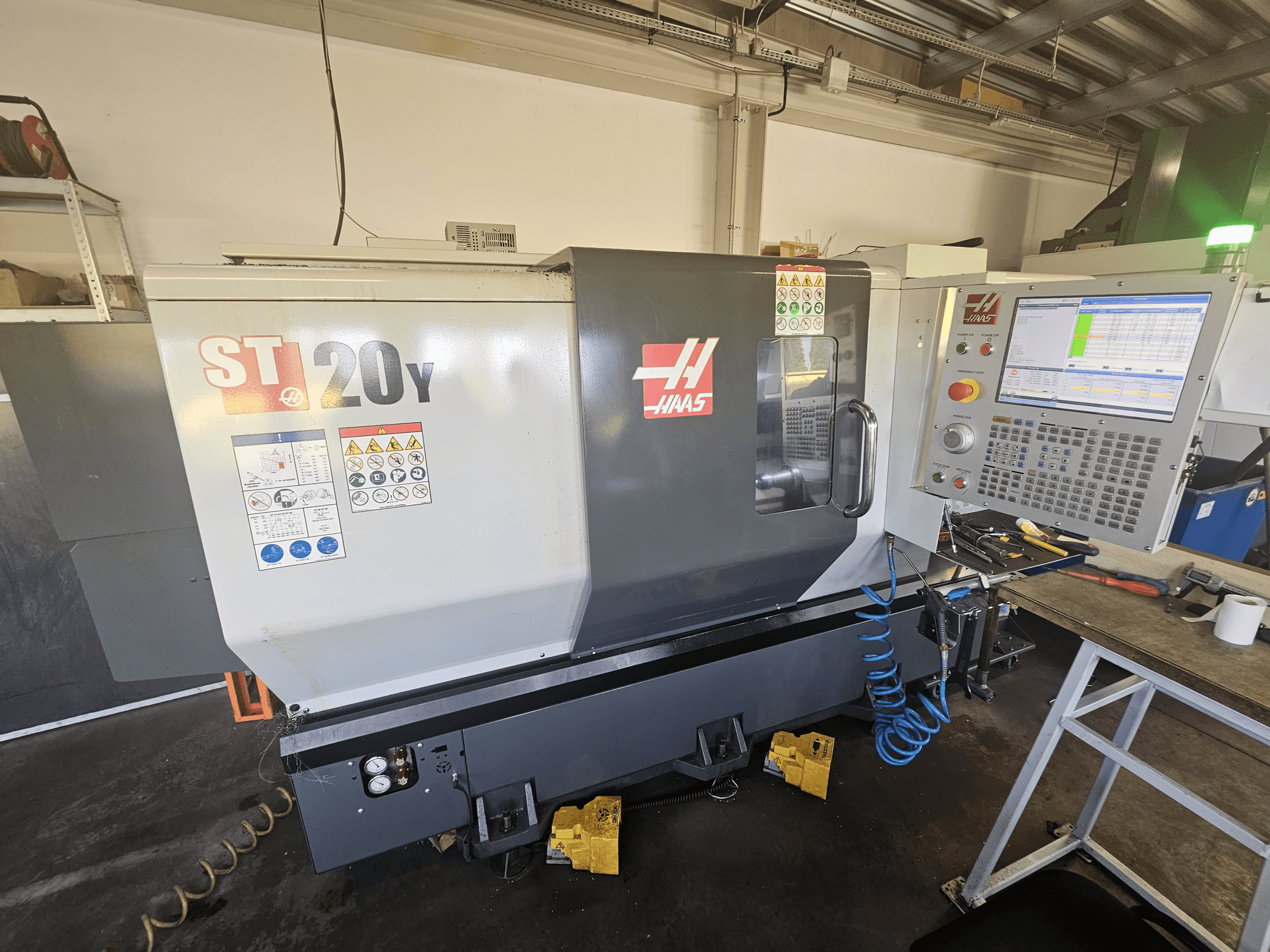 Haas ST-20Y CNC lathe in front view with control panel; includes safety labels and air hose detail on the side.