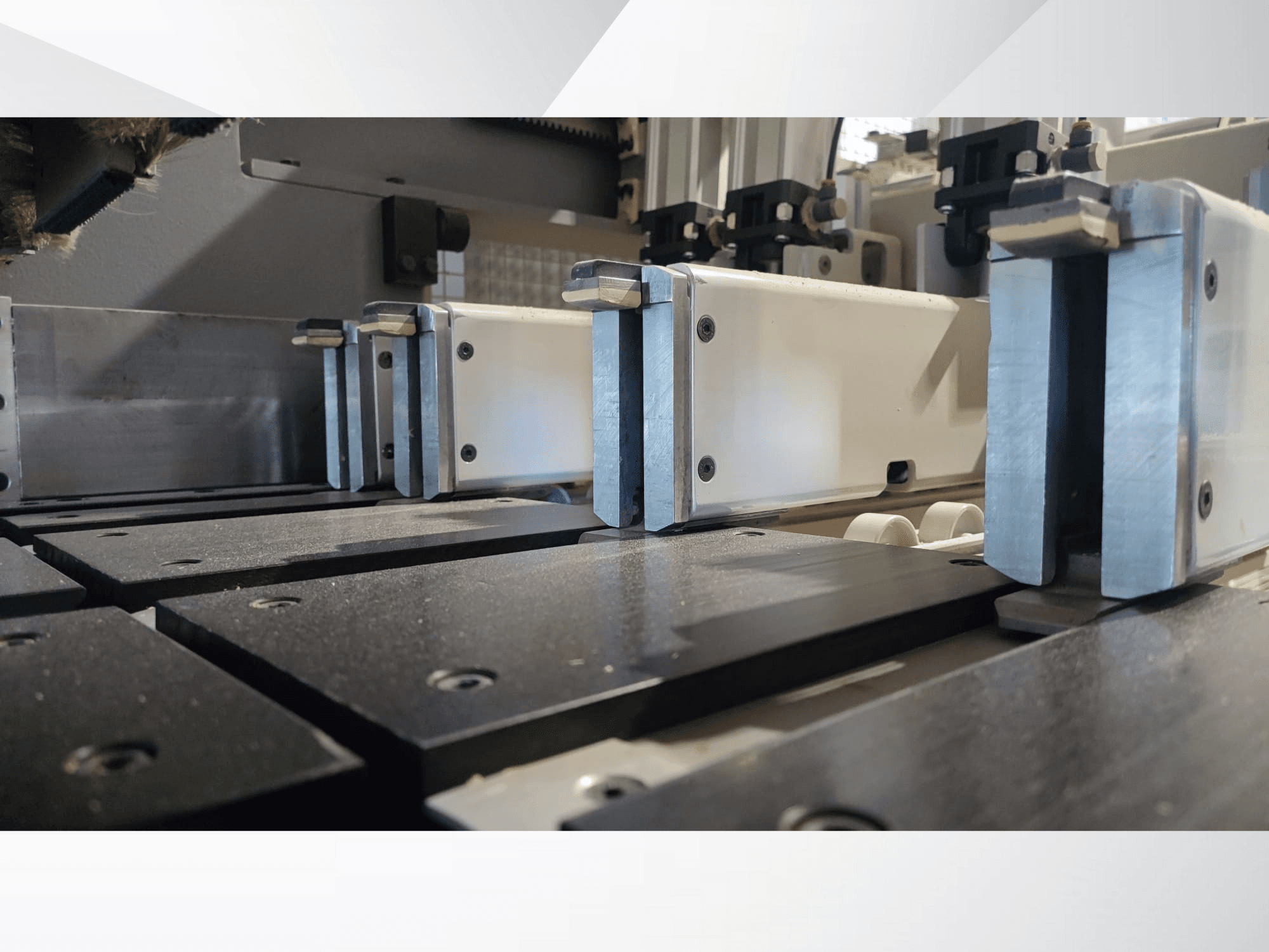 Close-up view of a precision machine's clamping mechanism with metallic jaws, featuring black work surfaces and visible guide rails.