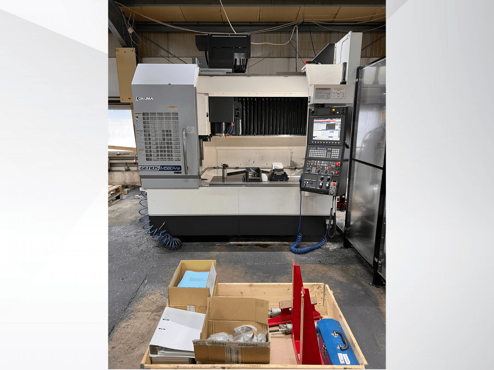 Okuma GENOS M460V-5 vertical machining center, front view, with control panel visible and tools on the worktable.