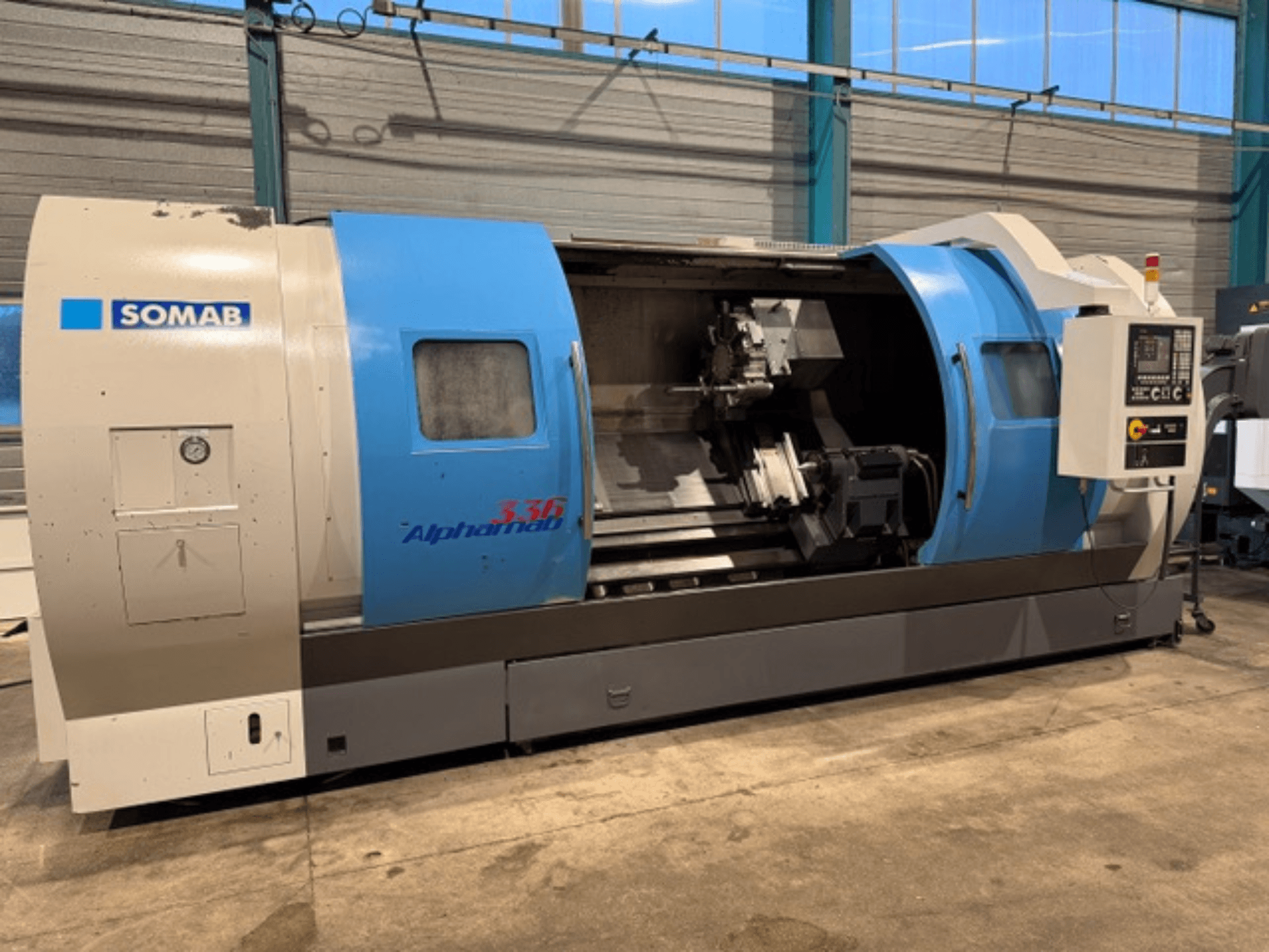 SOMAB Alpha 336 CNC lathe, front view, featuring blue and gray casing and a control panel on the side for operation.
