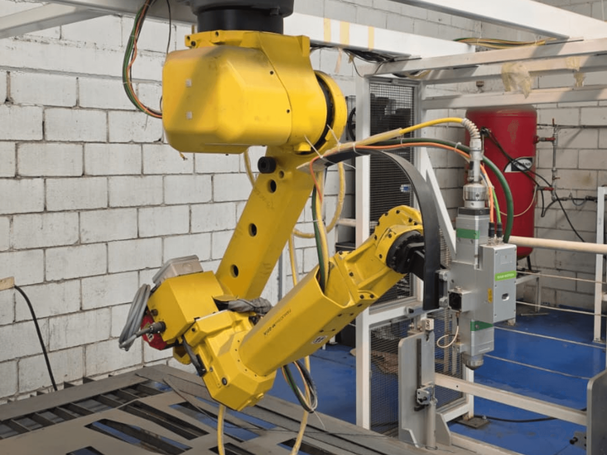 Yellow robotic arm with a precision tool, featuring multiple joints and cables, viewed from a front angle in an industrial setting.