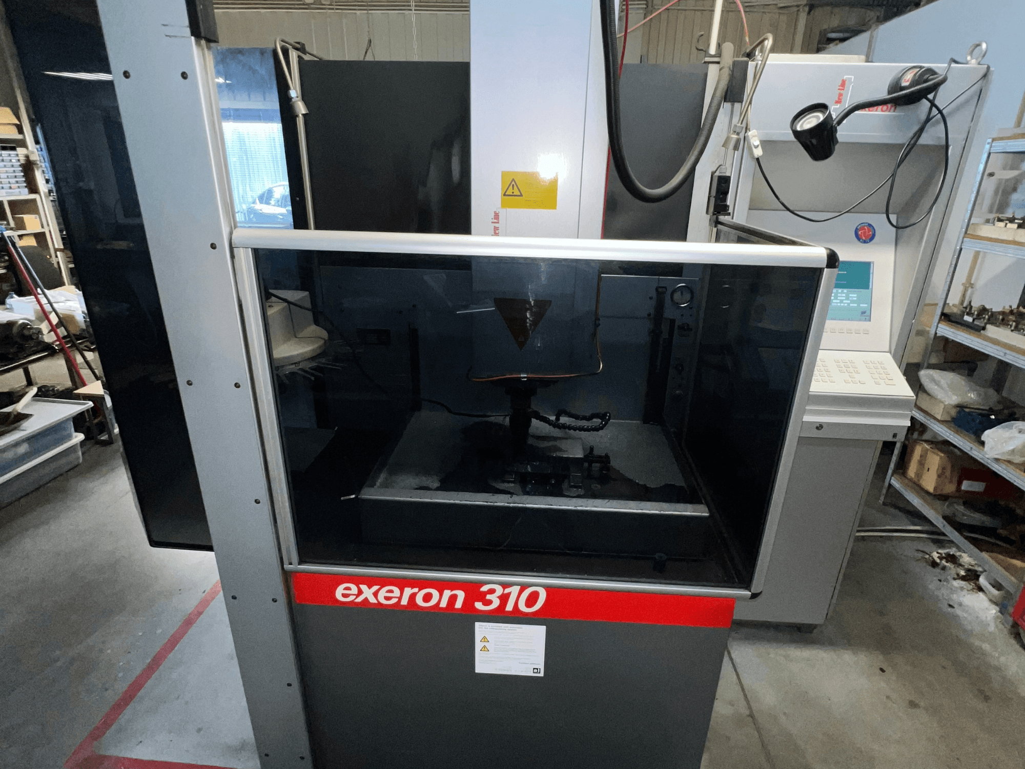 Front view of an Exeron 310 machine, showcasing a glass chamber and control panel alongside workstation shelving.