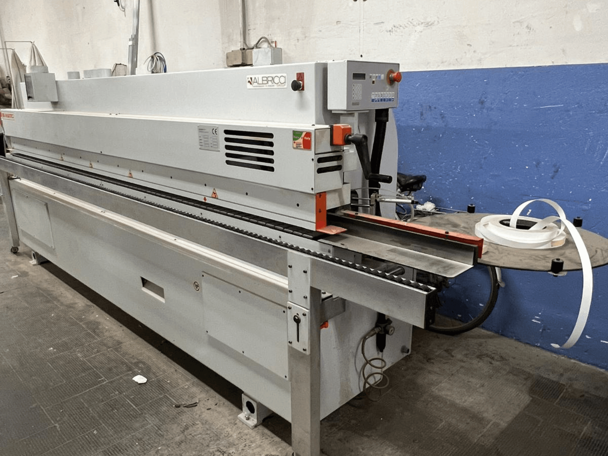 ALBRICO edge banding machine with a front view, featuring a long conveyor belt and an attached roll of adhesive tape.