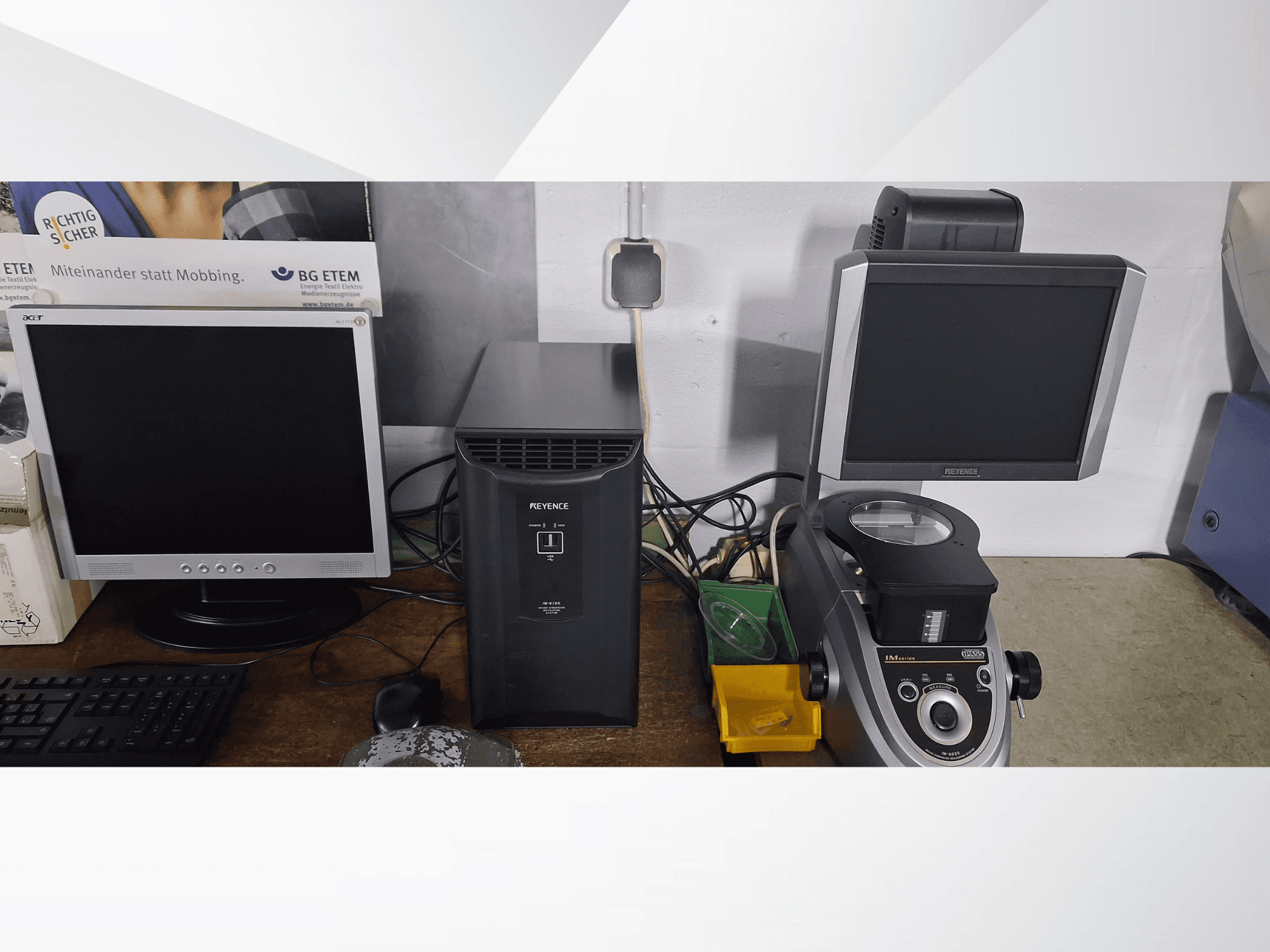 Two computer monitors, one Acer and one Keyence, next to a black device and a microscope, viewed from the front.