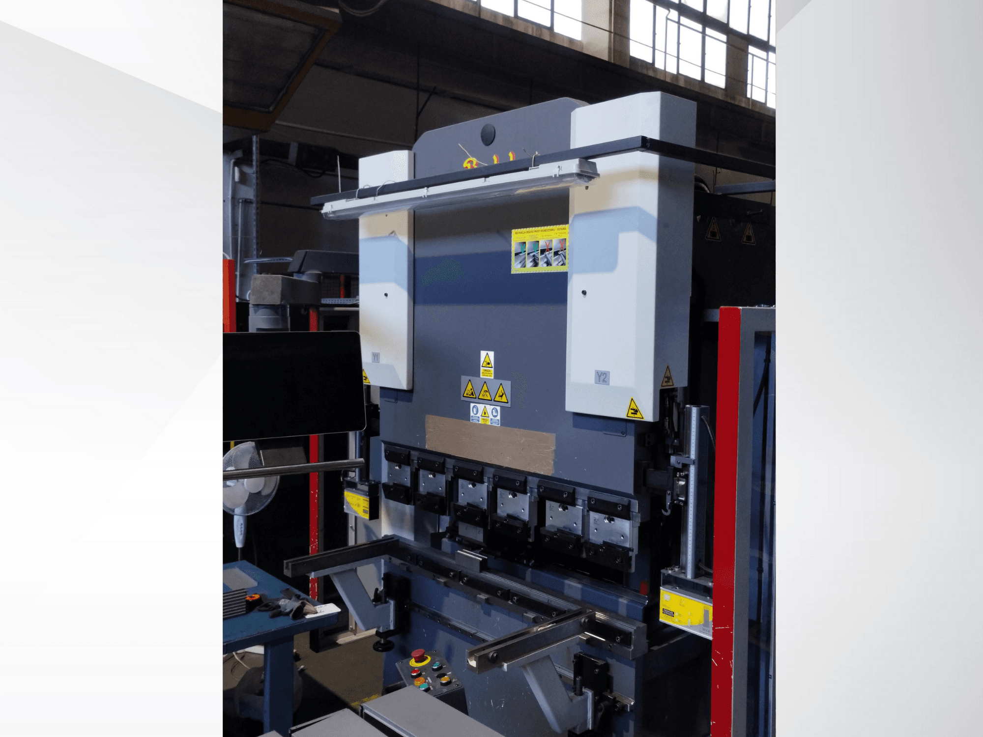 Press brake machine, front view. Features visible controls, safety stickers, and multiple die holders for precision bending.